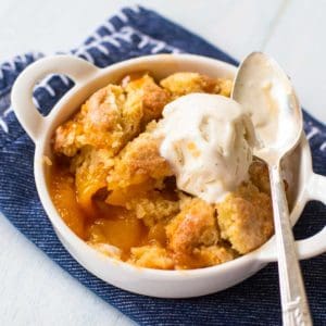 A dish of peach cobbler with a scoop of vanilla ice cream on top and a spoon.