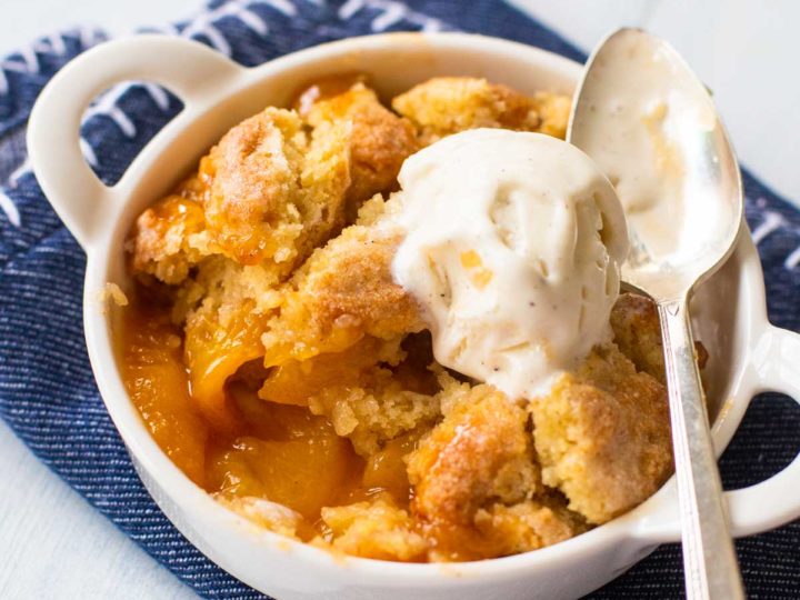 A dish of peach cobbler with a scoop of vanilla ice cream on top and a spoon.