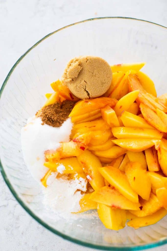 A bowl of fresh peaches with the sugars and seasonings to make pie filling.