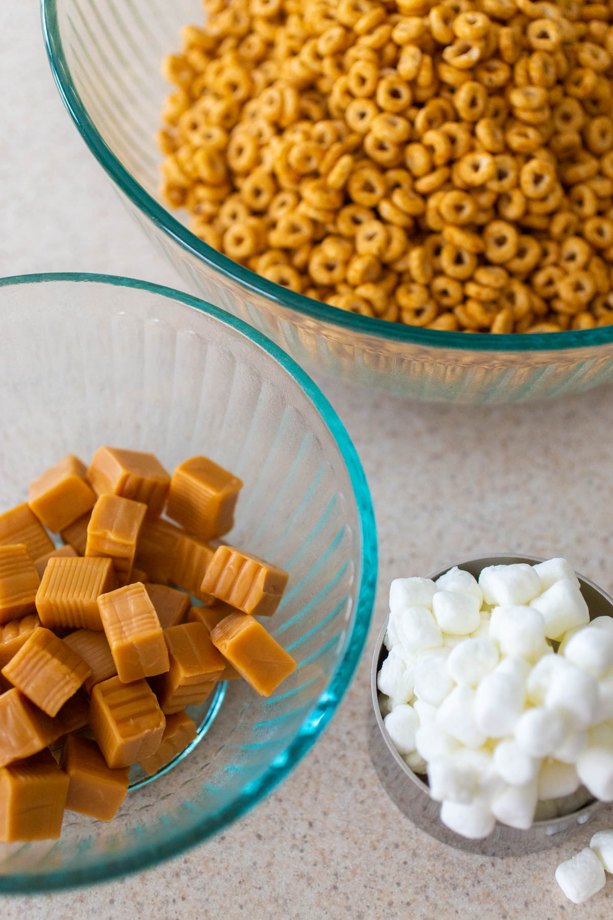The Pumpkin Spice Cheerios cereal is in a mixing bowl next to caramel candies and marshmallows.