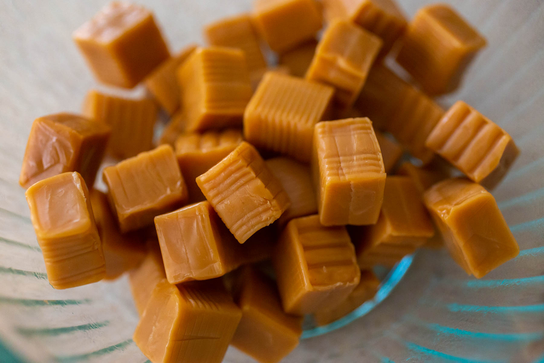 A glass mixing bowl has unwrapped caramel candies ready for melting.