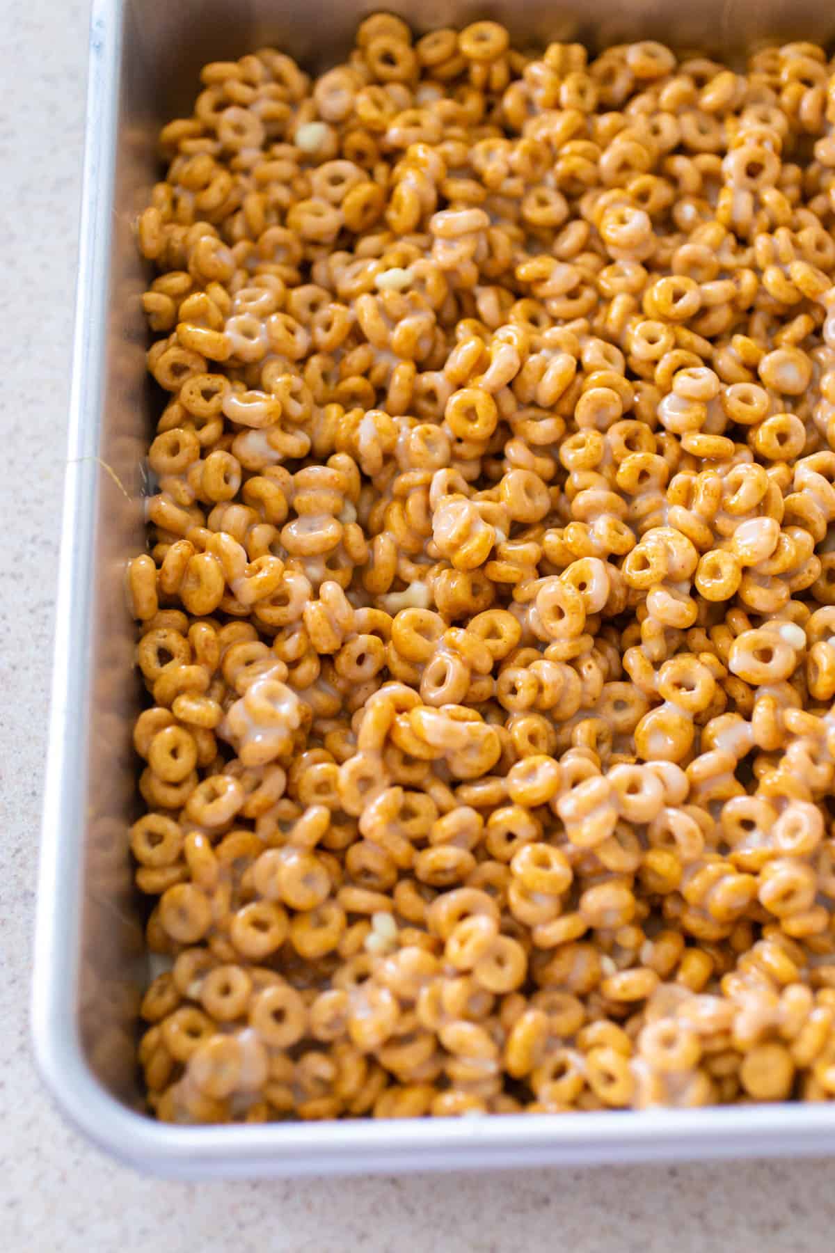 The Pumpkin Spice Cheerios bars have been spread into a 9x13-inch baking pan in an even layer.