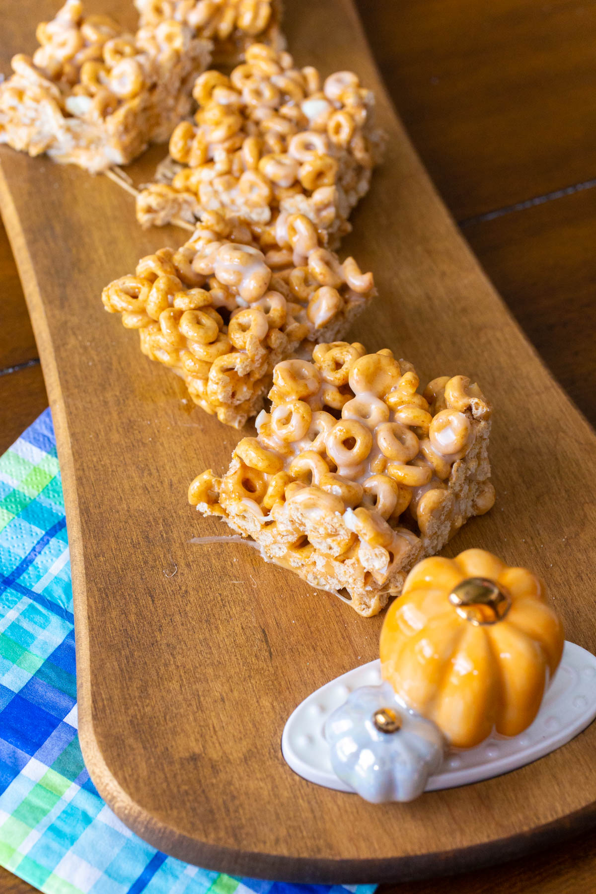 The sliced squares of Pumpkin Spice Cheerios treats are on a wooden serving board with a pumpkin decoration.