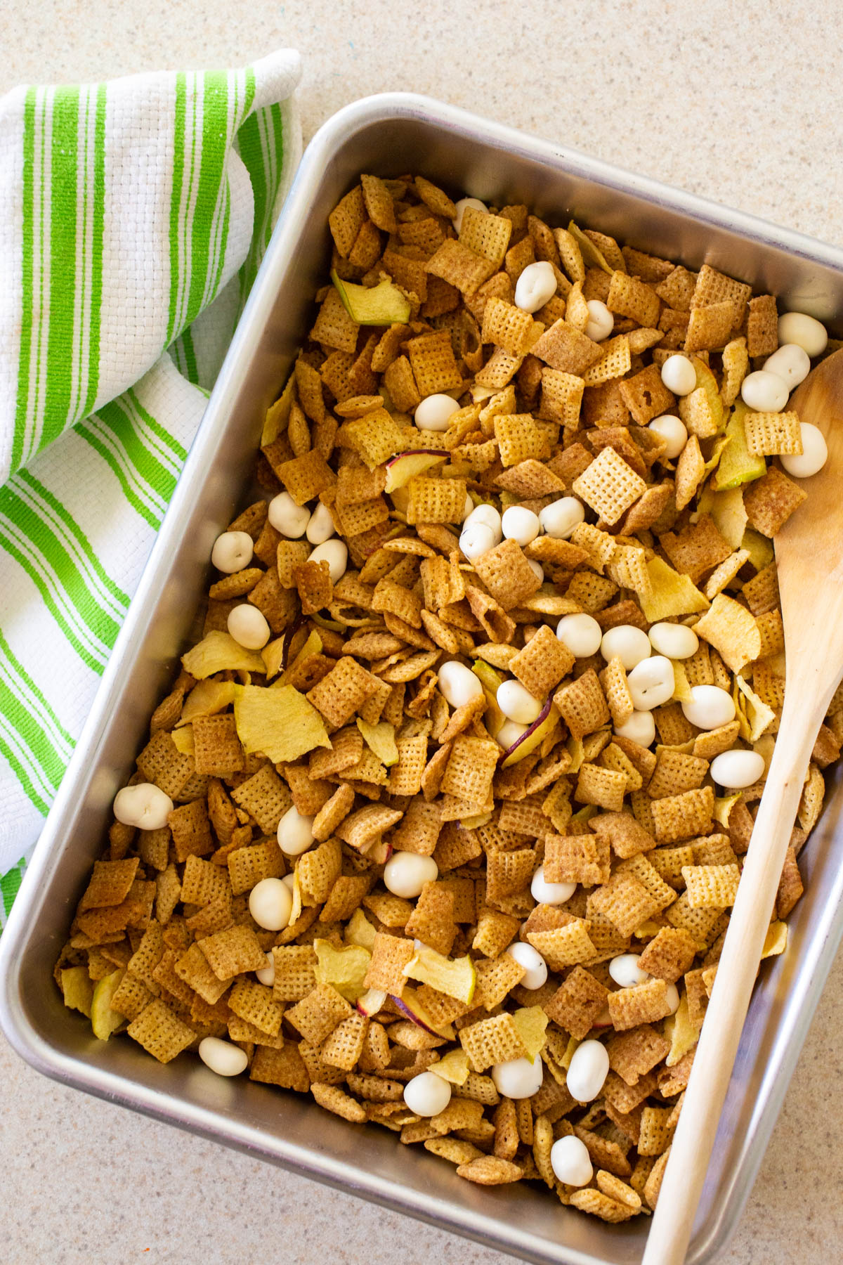 The finished snack mix is in a 9x13-inch metal pan with a spoon.