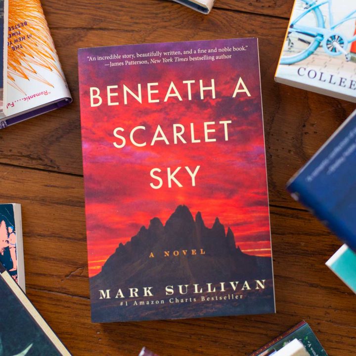A copy of Beneath a Scarlet Sky sits on a table.