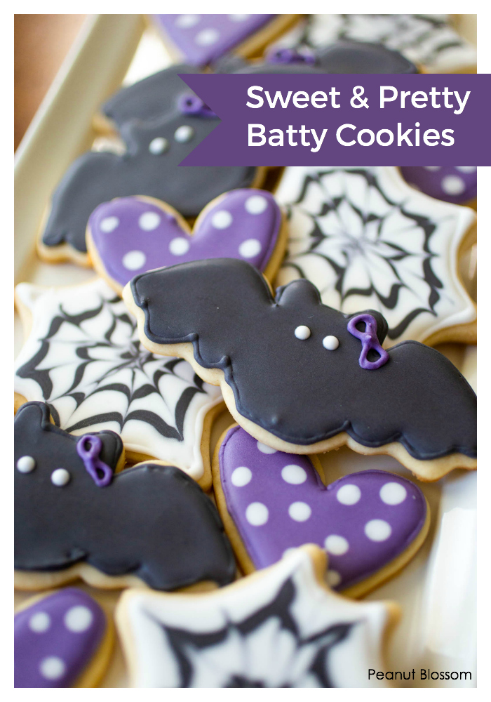 A sugar cookie platter has black bat cookies, black and white spider web cookies, and purple heart cookies with white polka dots.