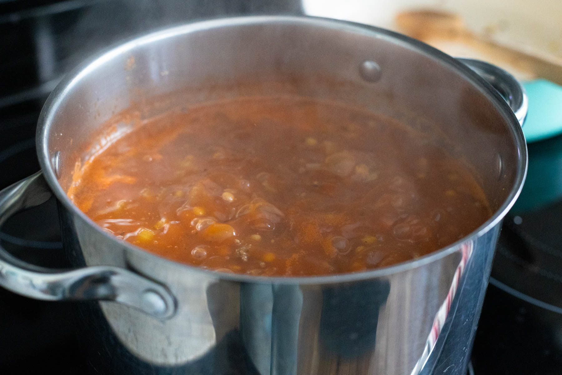 The soup pot is filled with the tomato-based soup and it is gently bubbling.