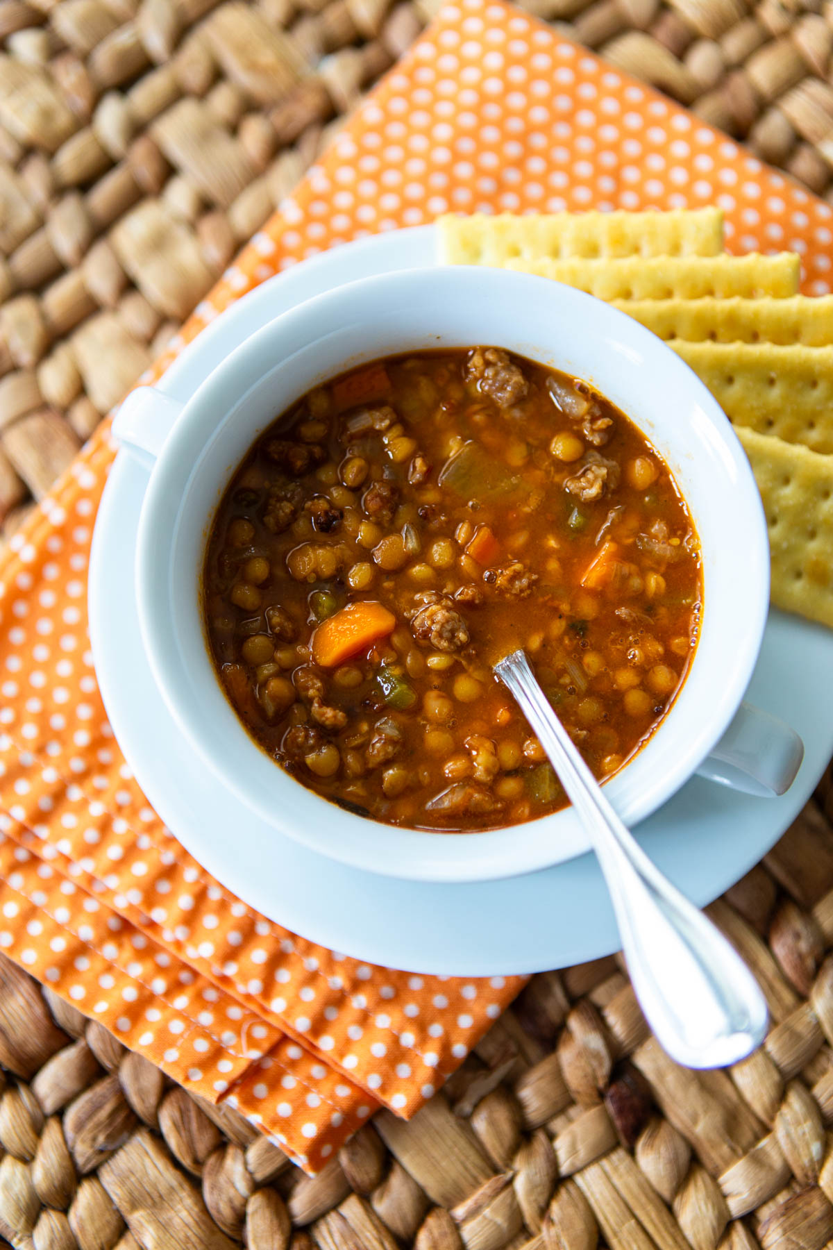 The sausage lentil soup is served in a white bowl alongside some crackers.