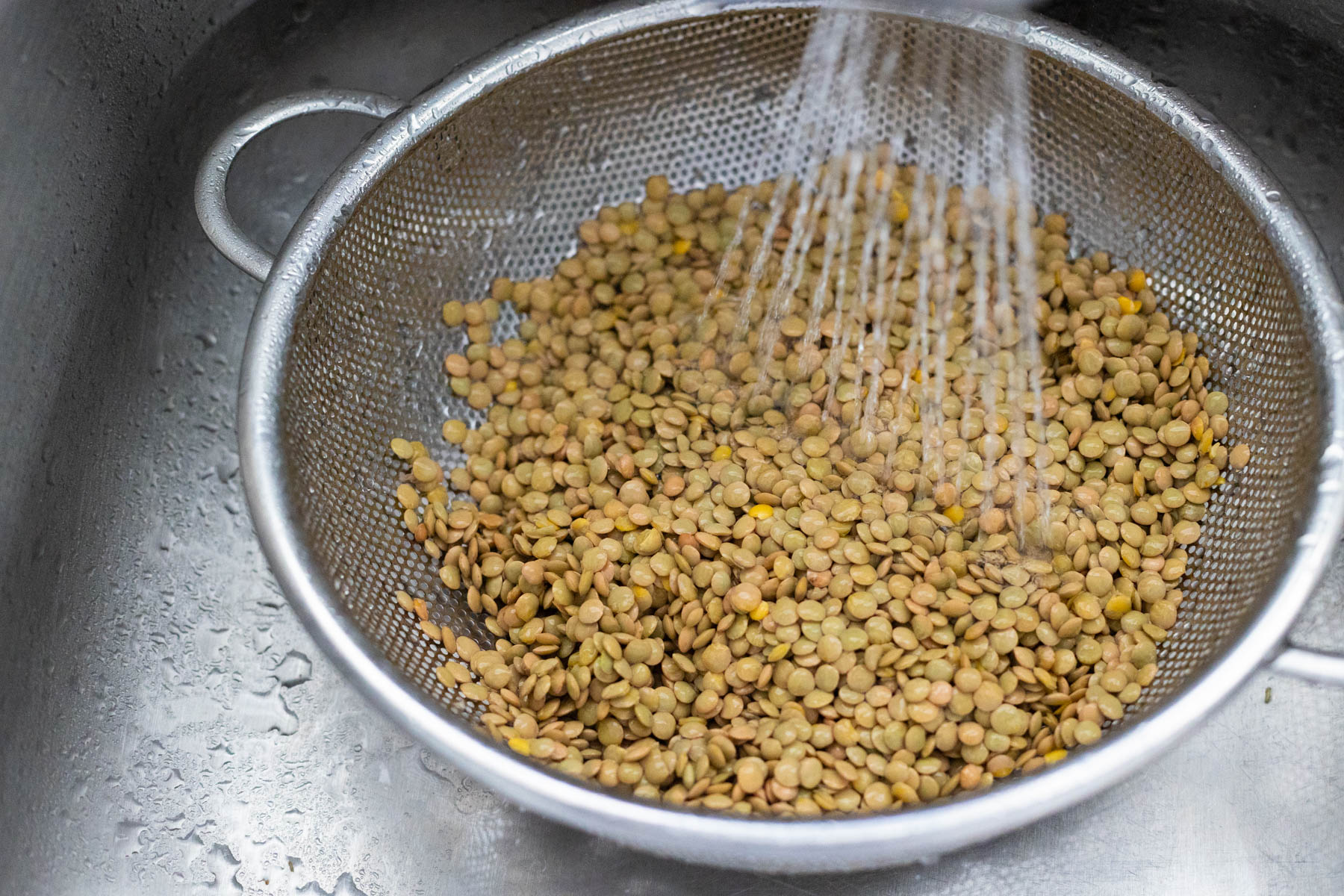 The lentils are in a strainer in the kitchen sink.