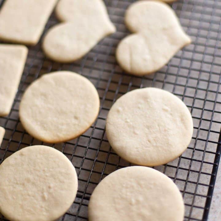 A wire rack has heart-shaped and circle-shaped undecorated sugar cookies cooling.