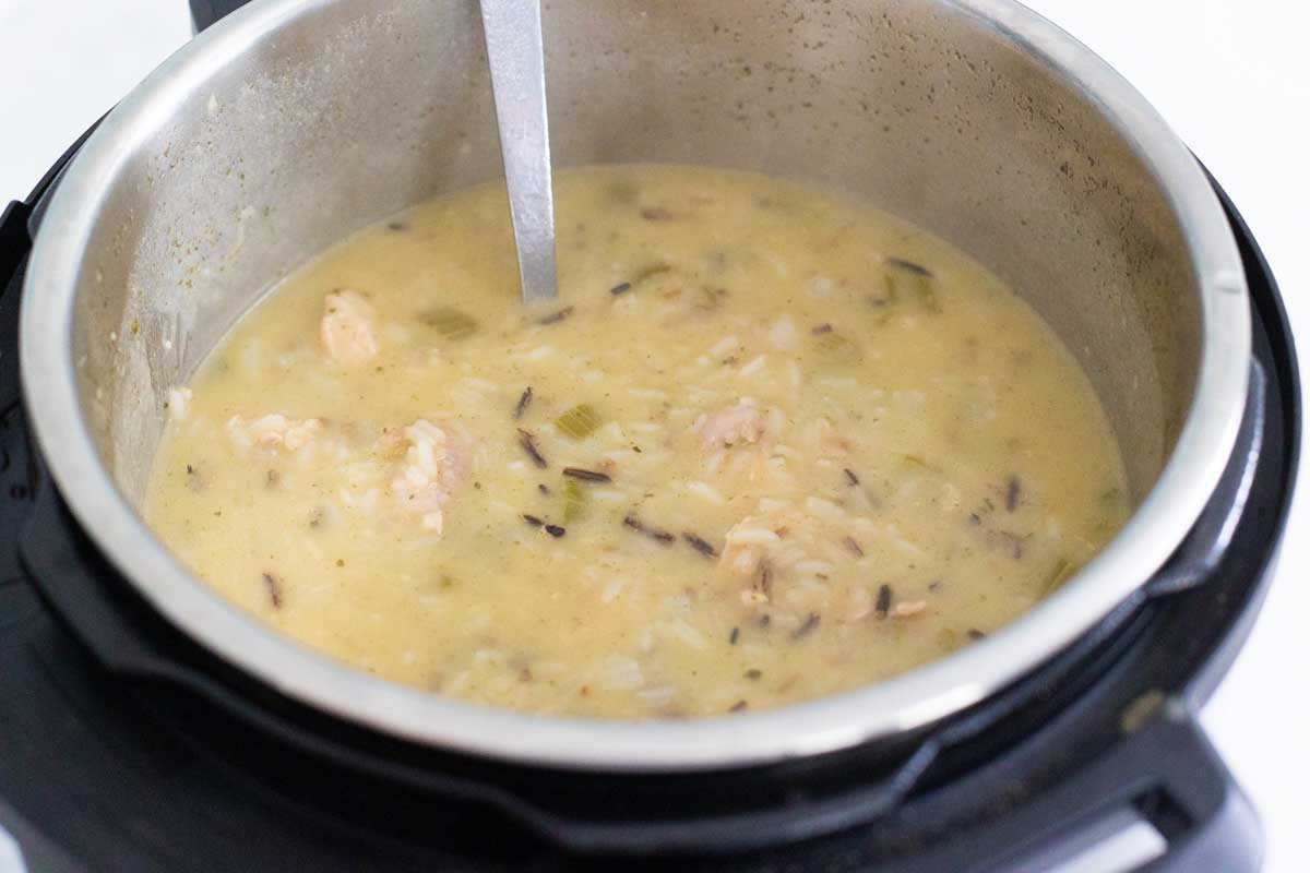 The Instant Pot chicken and rice soup is thick and creamy, there's a spoon stirring it right in the pot.