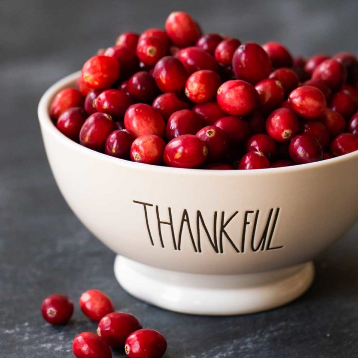 A bowl that says "Thankful" is filled with fresh cranberries.