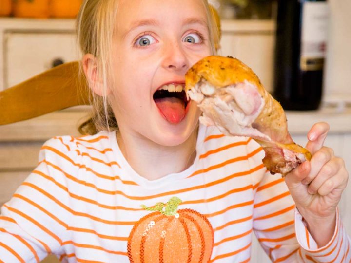 A young girl holds a giant turkey leg at the Thanksgiving table.