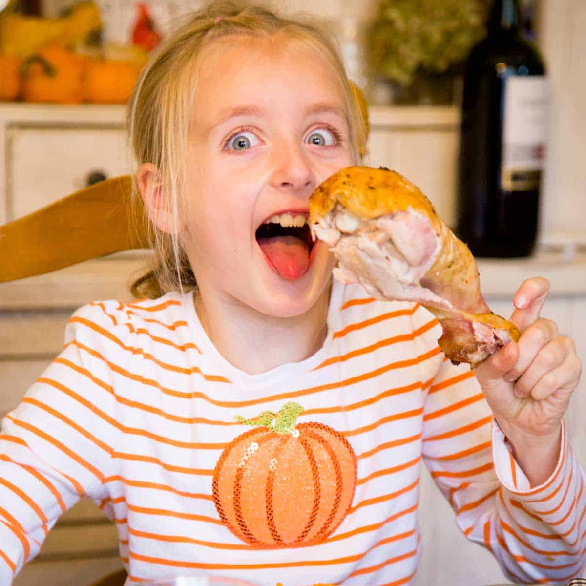 A young girl holds a giant turkey leg at the Thanksgiving table.