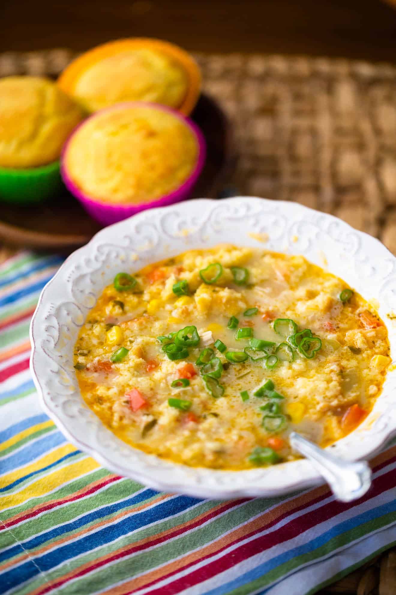 The soup is in a white bowl with a spoon, a plate of cornbread muffins in the background.