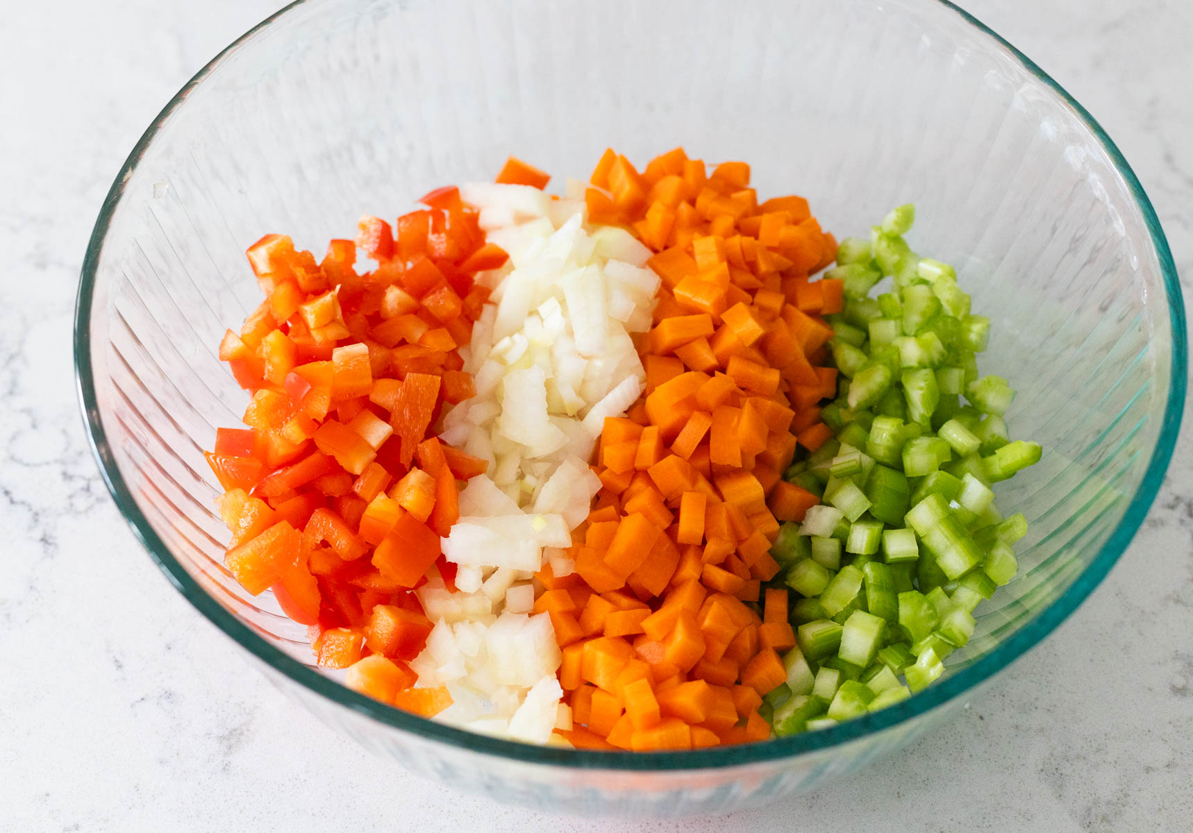 The mixing bowl has diced red peppers, onions, carrots, and celery.