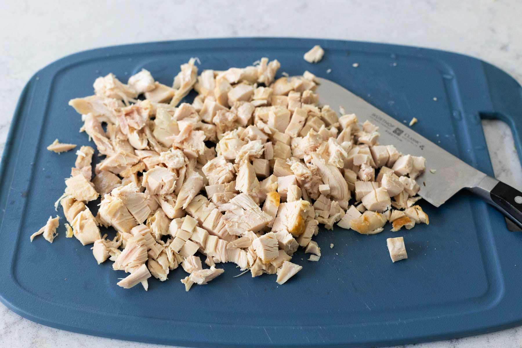 The rotisserie chicken meat has been pulled from the bone and finely diced on a cutting board.