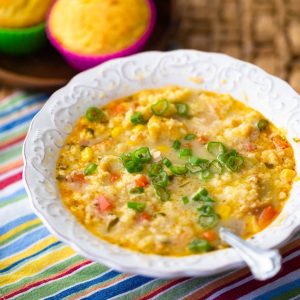 A bowl of caribbean chicken soup has fresh cilantro sprinkled over the top and corn bread muffins in the back.