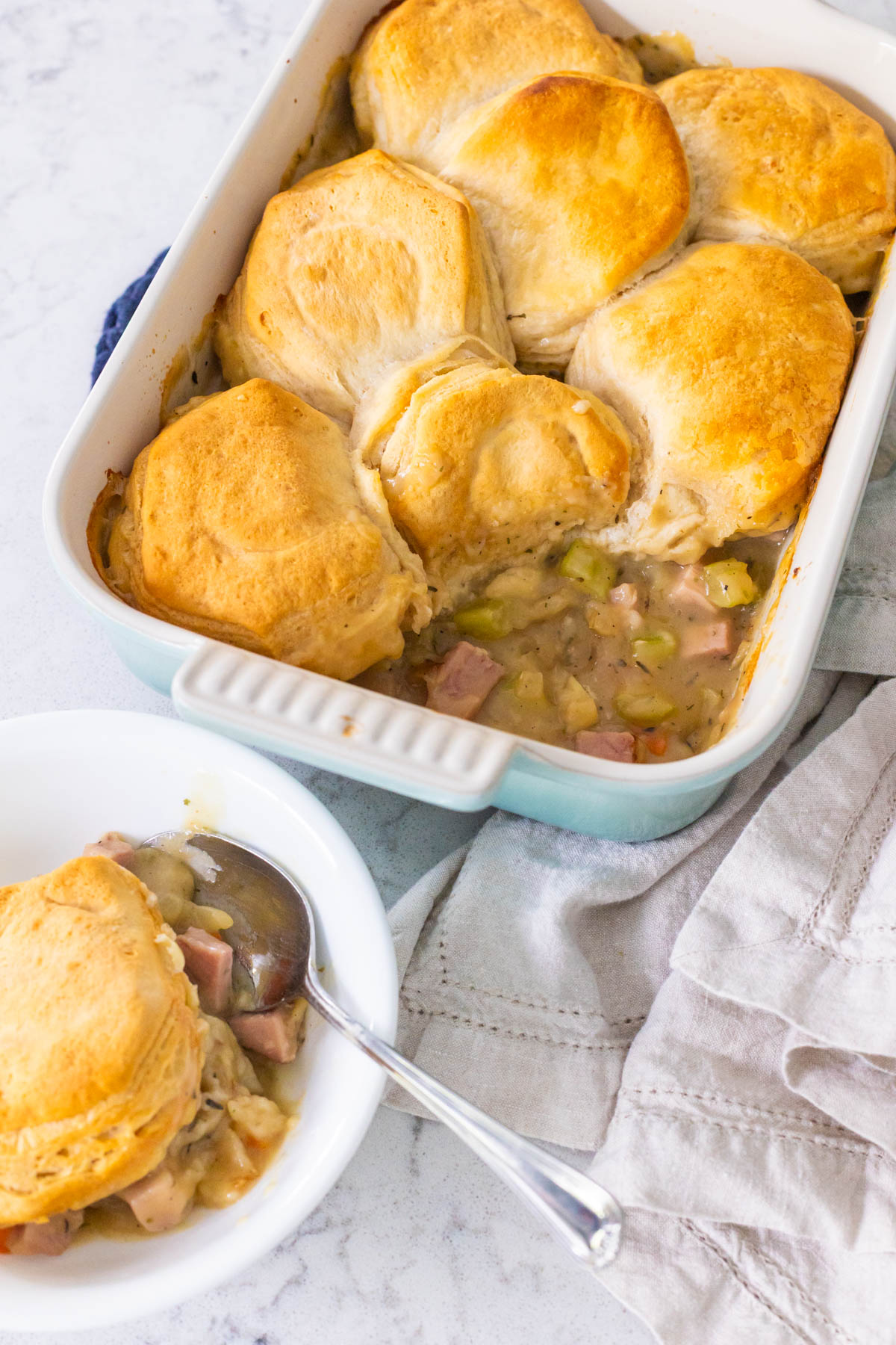 A blue baking dish is filled with ham pot pie with biscuits on top.