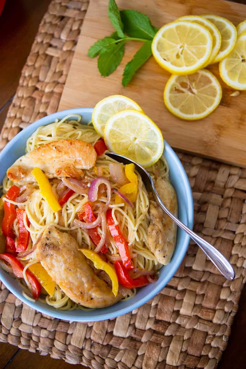 A blue bowl is filled with the chicken scampi pasta and is garnished with lemon slices.