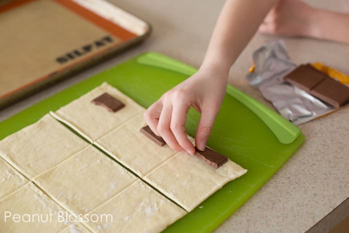 Squares of chocolate are being placed on one side of each square of dough.