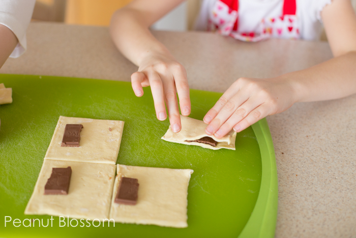 Each square of dough is being folded over to form a rectangle around the chocolate.