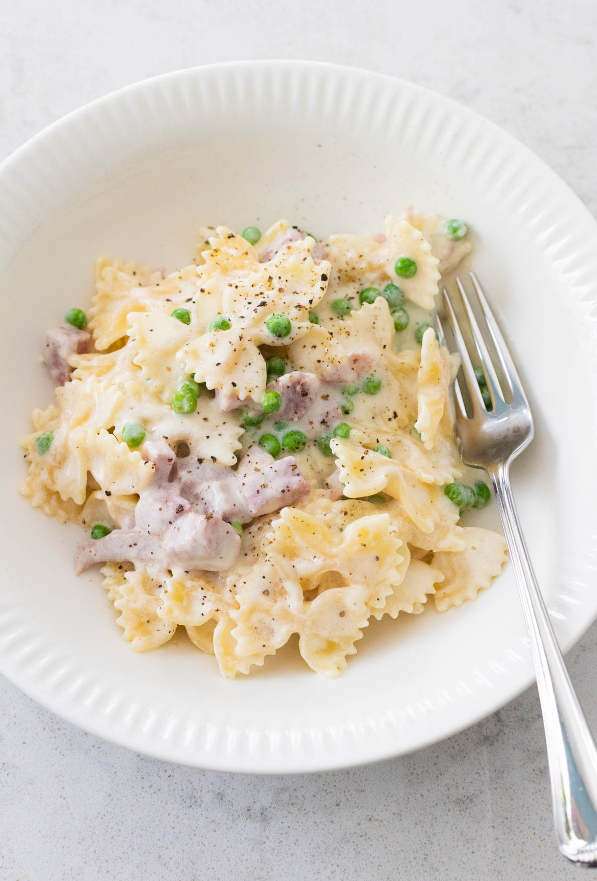 A white bowl filled with farfalle pasta, cubed ham, and peas to show the ham and peas alfredo recipe.