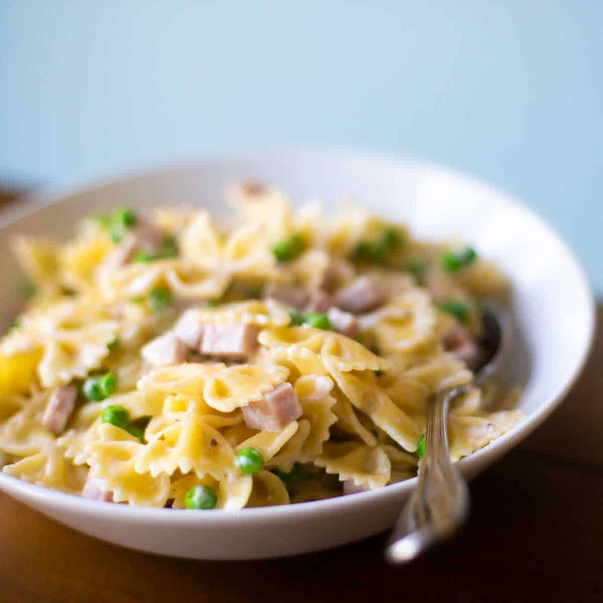 A white bowl filled with farfalle pasta, cubed ham, and peas to show the ham and peas alfredo recipe.