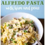 A bowl of alfredo pasta with ham and peas and a fork.