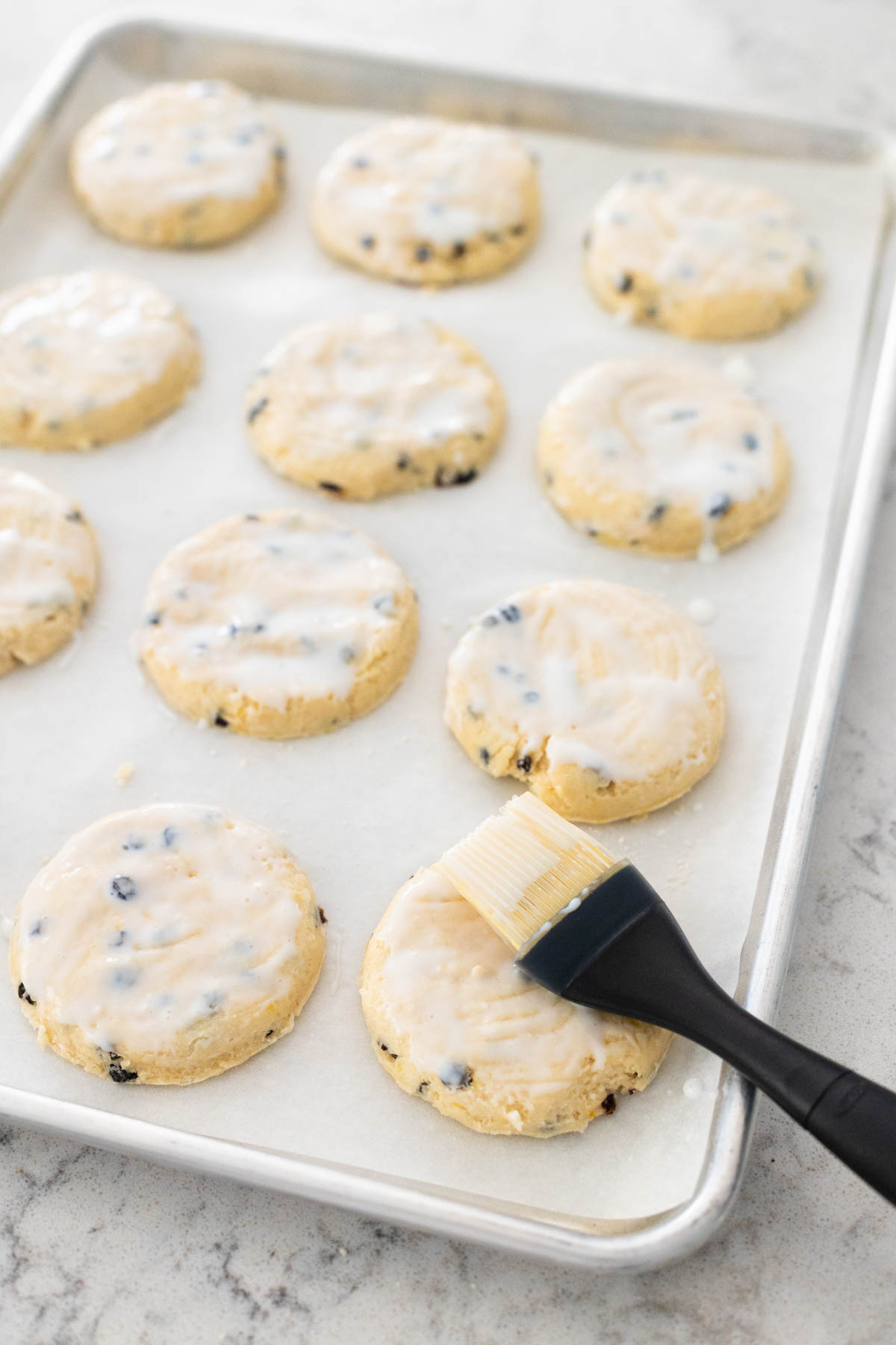 The pastry brush is brushing buttermilk over the top of the biscuits before baking.