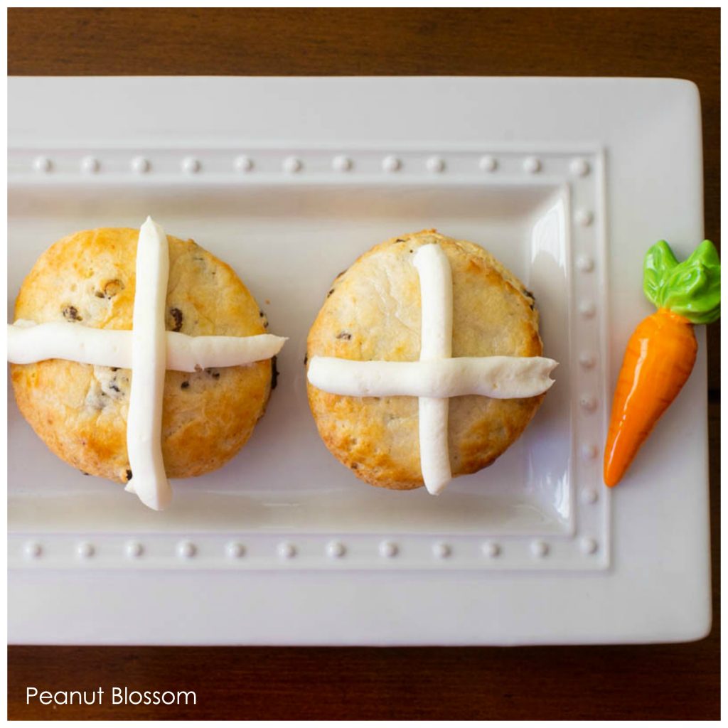 Two hot cross biscuits are on a platter with a ceramic carrot decoration on the side.