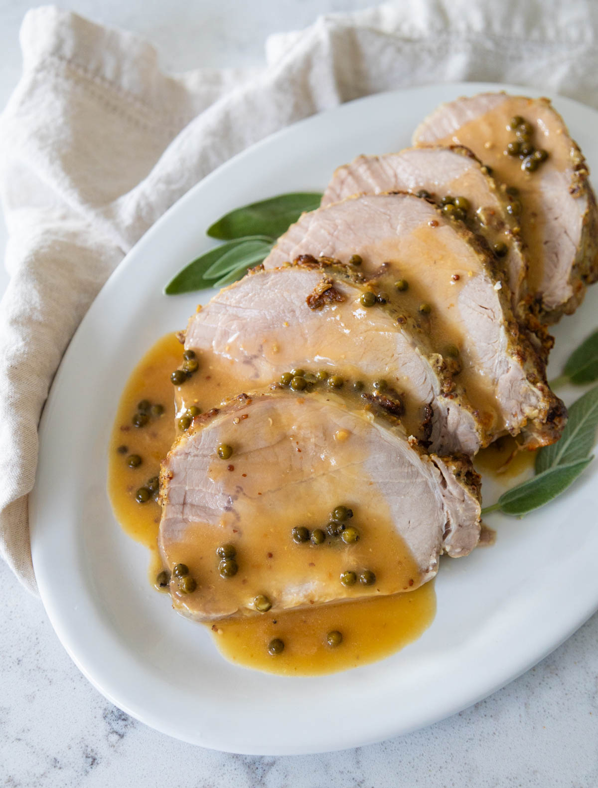 The sliced pork is served with a drizzle of green peppercorn sauce.