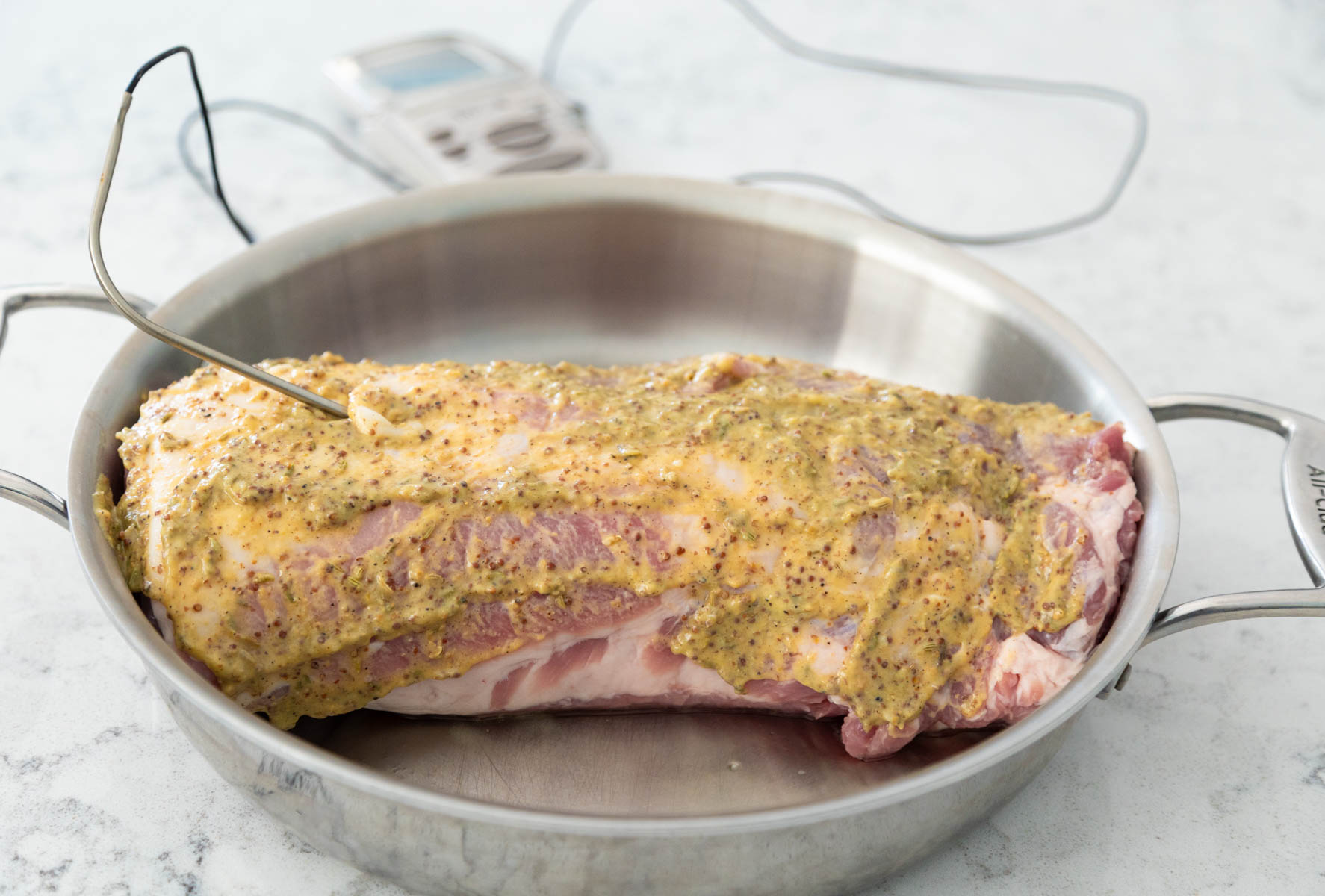 The pork loin is in a large saute pan and has been rubbed down with a mustard glaze.
