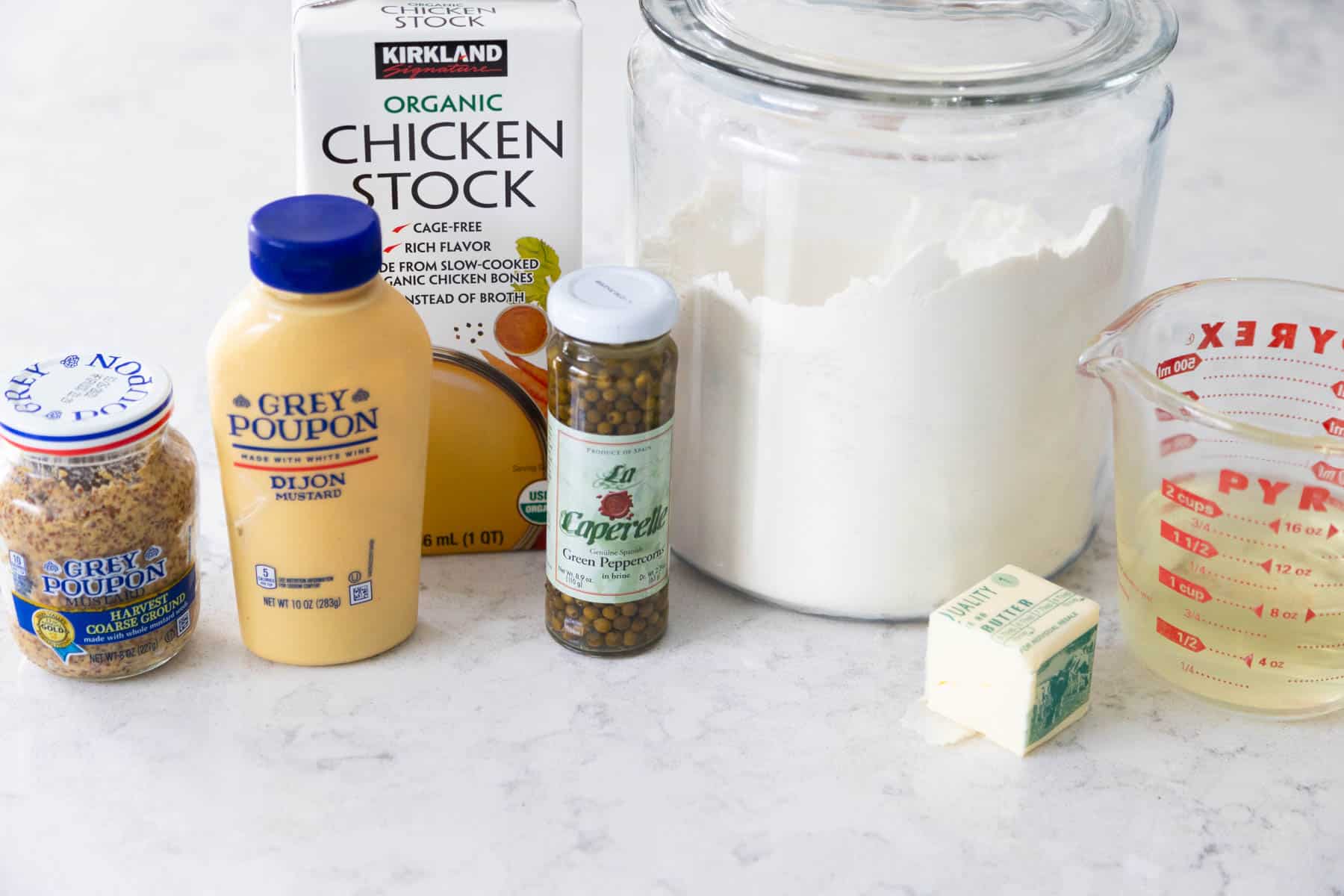 The bottle of green peppercorns is on the counter next to the remaining ingredients to make the sauce.