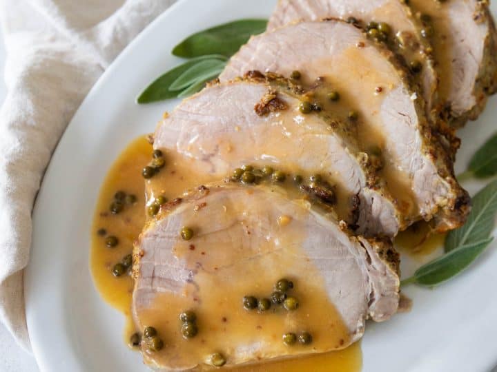 The roasted pork loin is served on a platter with a drizzle of green peppercorn sauce.