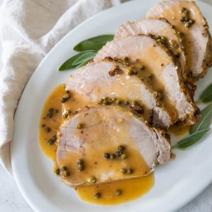 The roasted pork loin is served on a platter with a drizzle of green peppercorn sauce.