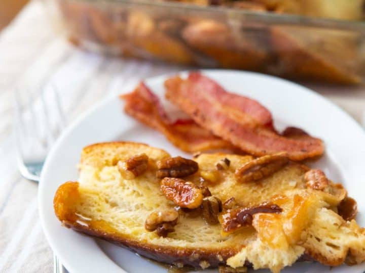 A serving of French toast casserole topped with pecans has slices of bacon on the side.
