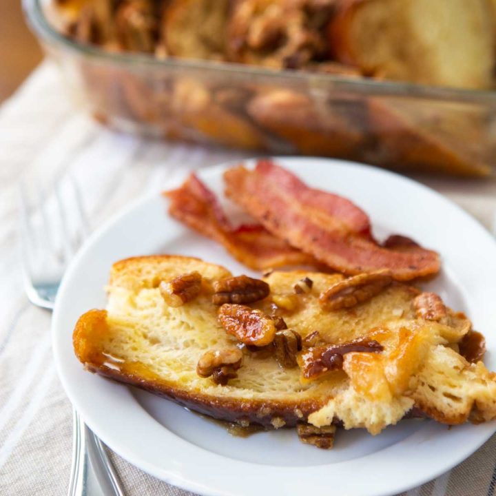 A serving of French toast casserole topped with pecans has slices of bacon on the side.