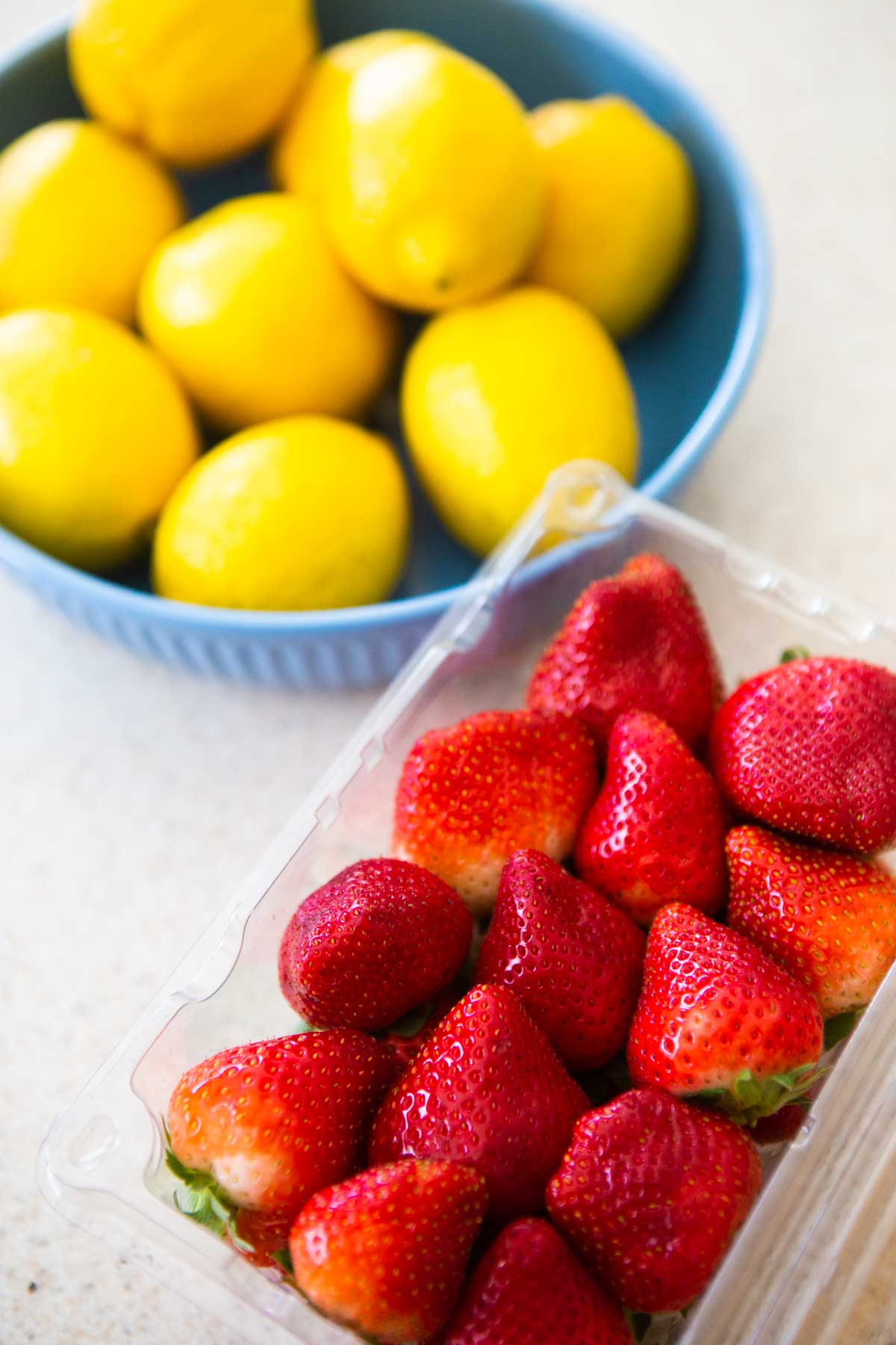 A bowl of lemons is next to a container of fresh strawberries.