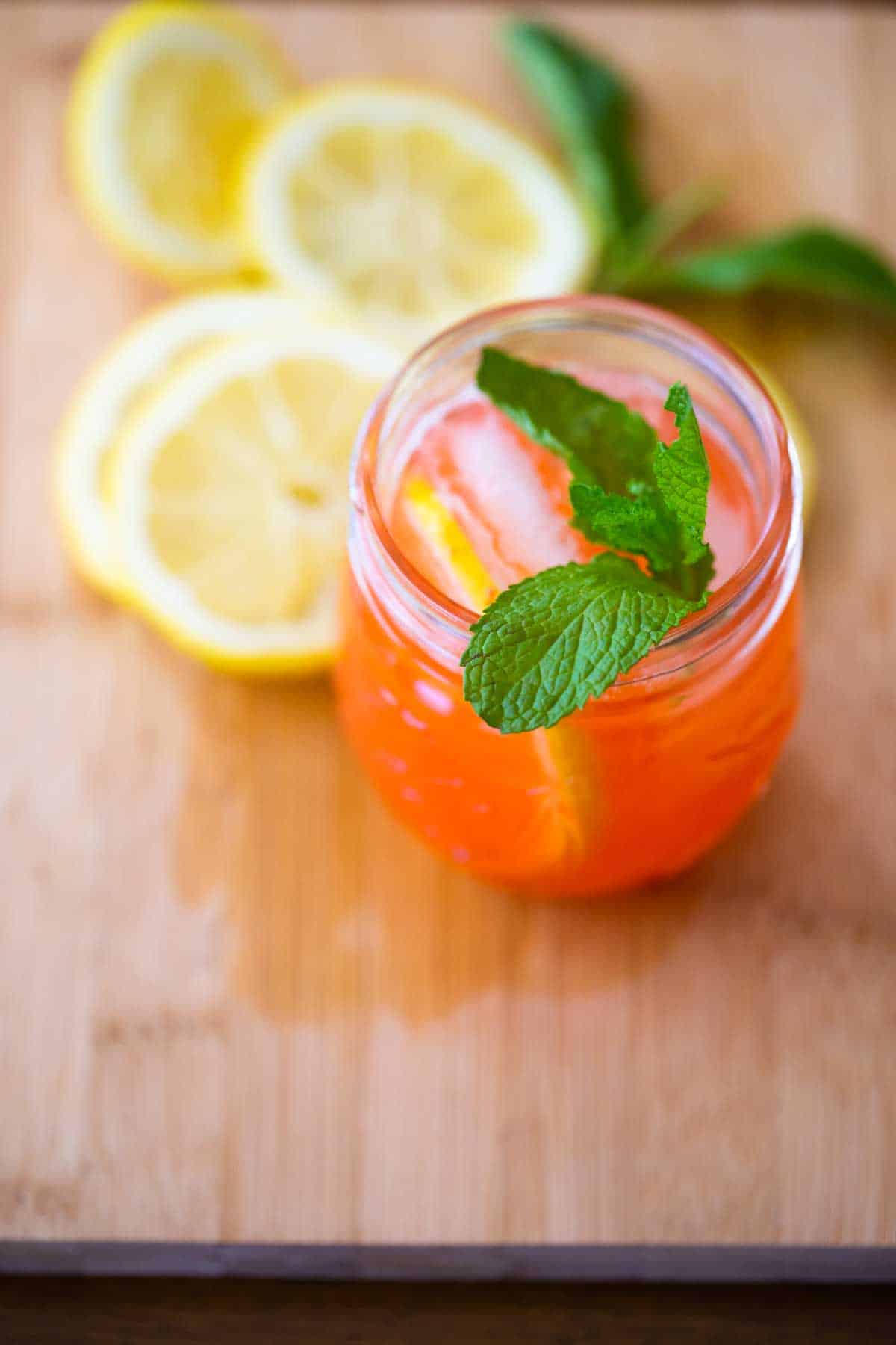 The glass of lemonade has been garnished with fresh. mint. Lemon slices sit next to the glass.