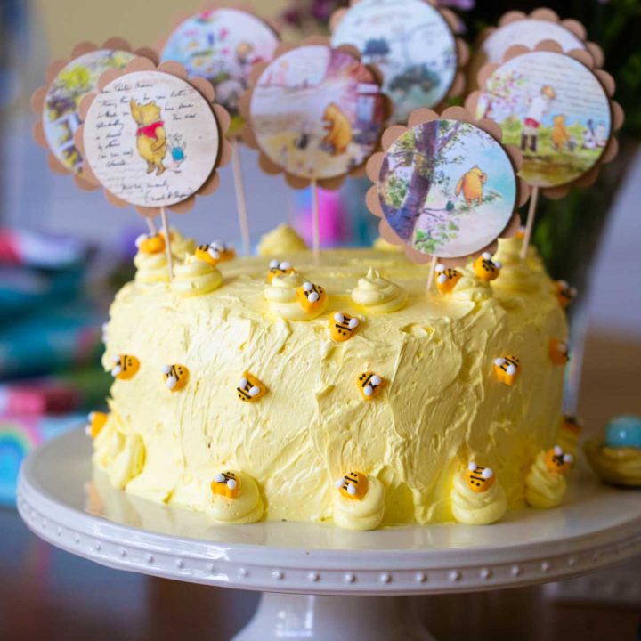 Adorable yellow Winnie the Pooh cake features tiny bees and several Pooh-themed cake picks on top.
