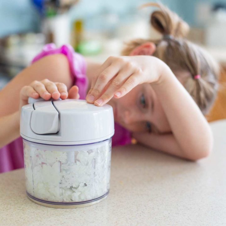A young girl chops onions in a food processor.
