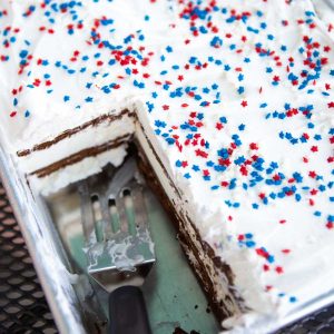 A metal pan has an ice cream cake with red and white sprinkles over the top. A slice is missing so you can see the layers of ice cream sandwiches inside.
