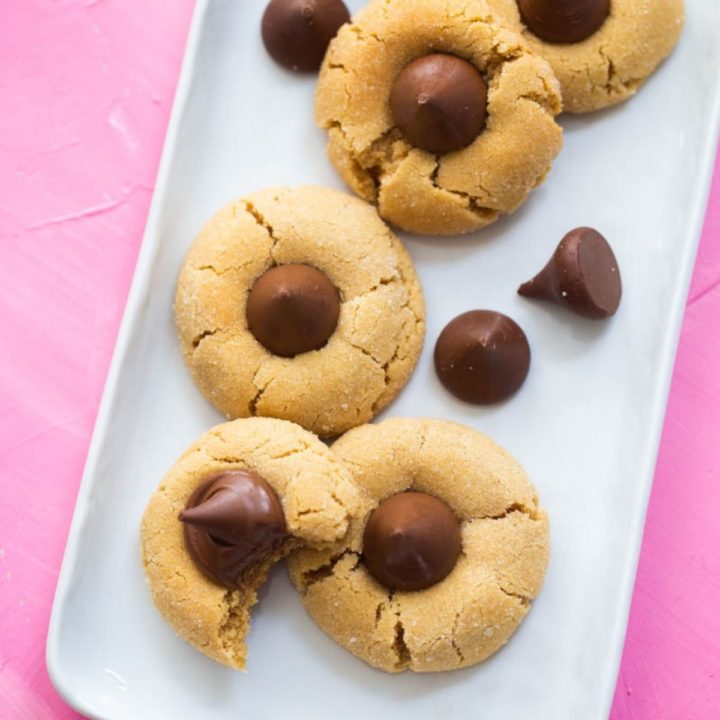 Peanut butter blossom cookies are on a white tray on a pink background.