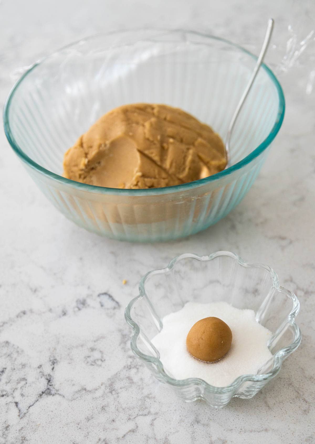 The bowl of cookie dough is in the back, a single rolled ball of cookie dough is in a bowl of sugar in the front.