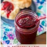 The jar of blackberry jam is next to a biscuit.