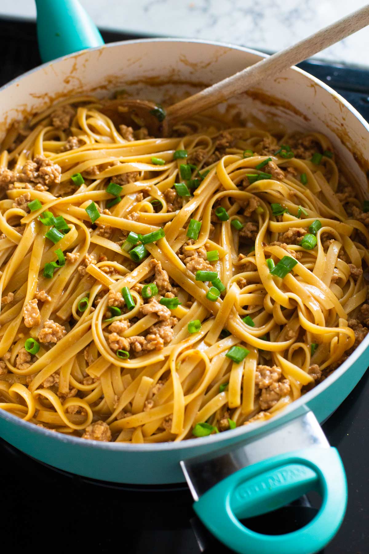 A pan filled with the finished peanut butter noodles topped with green onions.