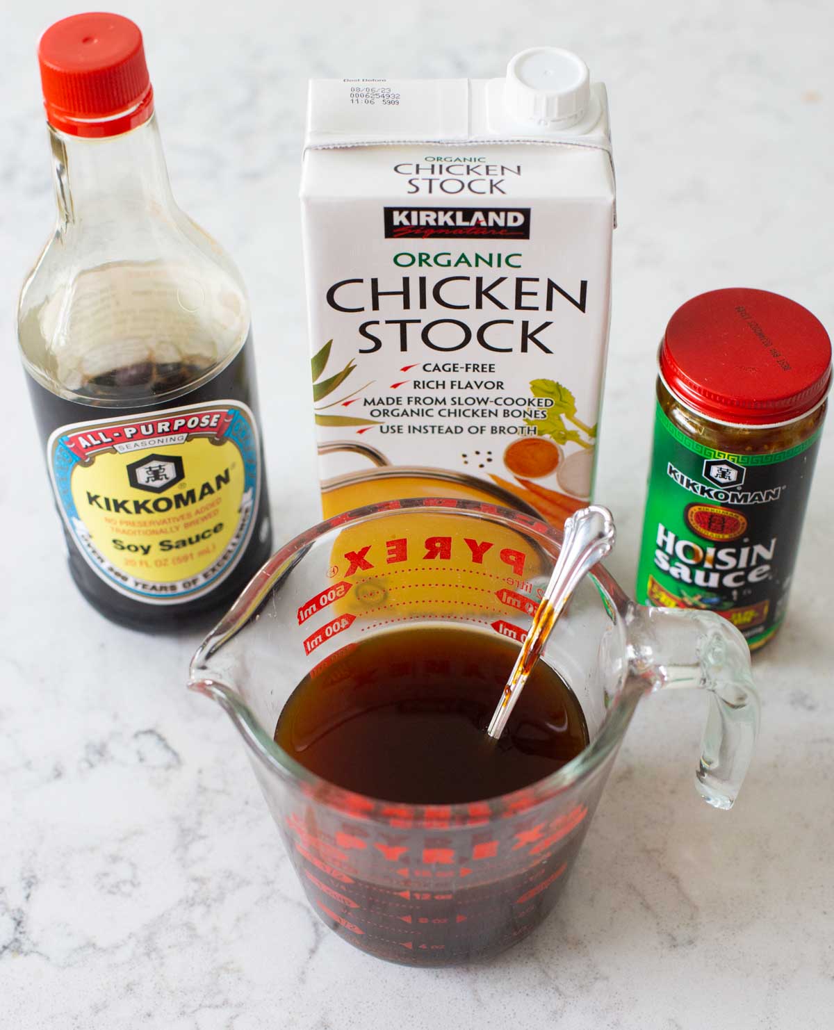 Chicken stock, soy sauce, and hoisin sauce are mixed together in a measuring cup.