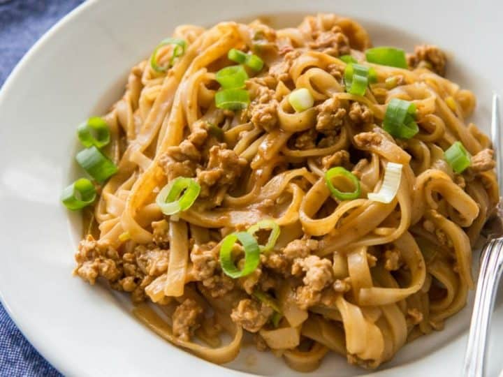 A serving of Chinese noodles with ground pork has green onions sprinkled over the top.