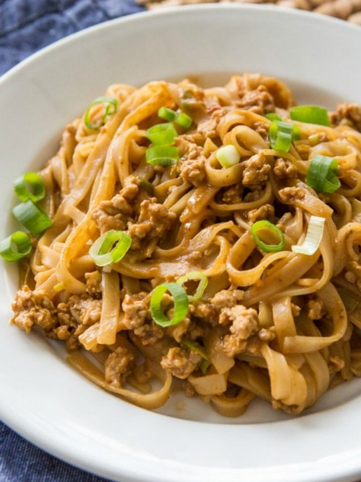 A serving of Chinese noodles with ground pork has green onions sprinkled over the top.